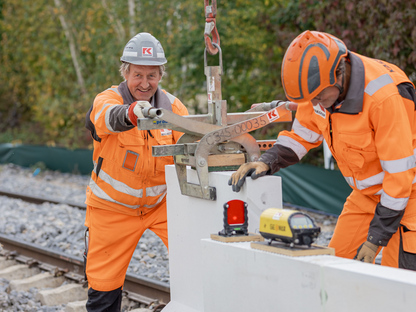 KASSECKER Vorarbeiter im Bahn- und Ingenieurbau bei Arbeiten am Gleis. Er trägt orange Arbeitskleidung und einen grauen Helm mit KASSECKER Logo.