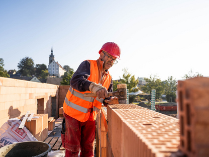 Baustellenmitarbeiter setzt einen Ziegelstein auf eine Mauer