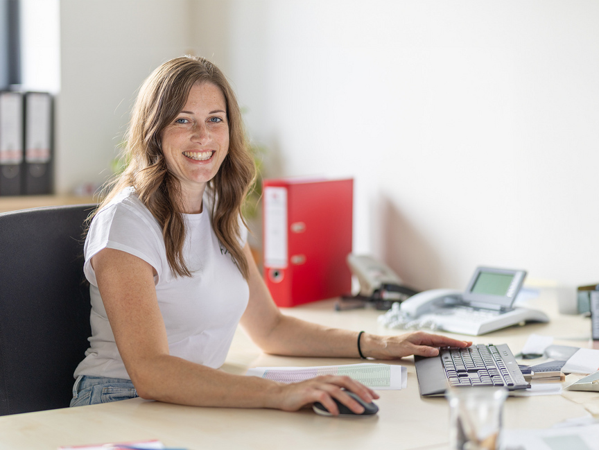 Frau sitzt an einem Schreibtisch und hat eine Computermaus in der Hand.